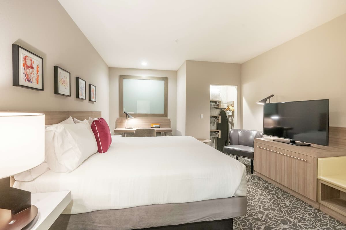 A hotel room with a bed, a desk, a TV, and a bathroom visible in the background.