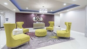 Een moderne lobby met een kroonluchter, gele fauteuils, een rond poef en een decoratieve spiegelwand.