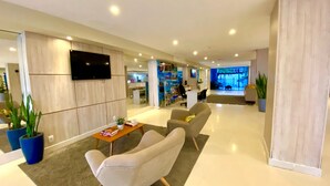 Un moderno vestíbulo de hotel con un televisor de pantalla plana, asientos cómodos, una recepción y una gran pantalla digital.