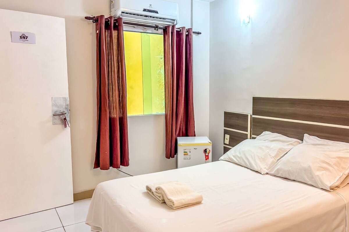 Ein Hotelzimmer mit Bett, einem Fenster mit Vorhängen, einer Klimaanlage und einem kleinen Kühlschrank.