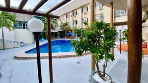 Un área de piscina con piscina azul cristalina, rodeada de plantas en macetas y mobiliario de exterior.