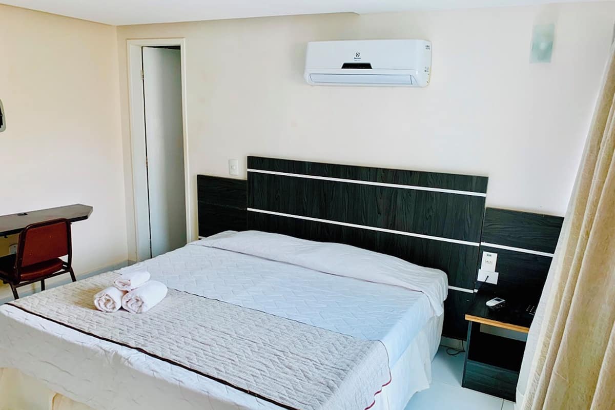 A hotel room with a bed, a desk, and an air conditioning unit.