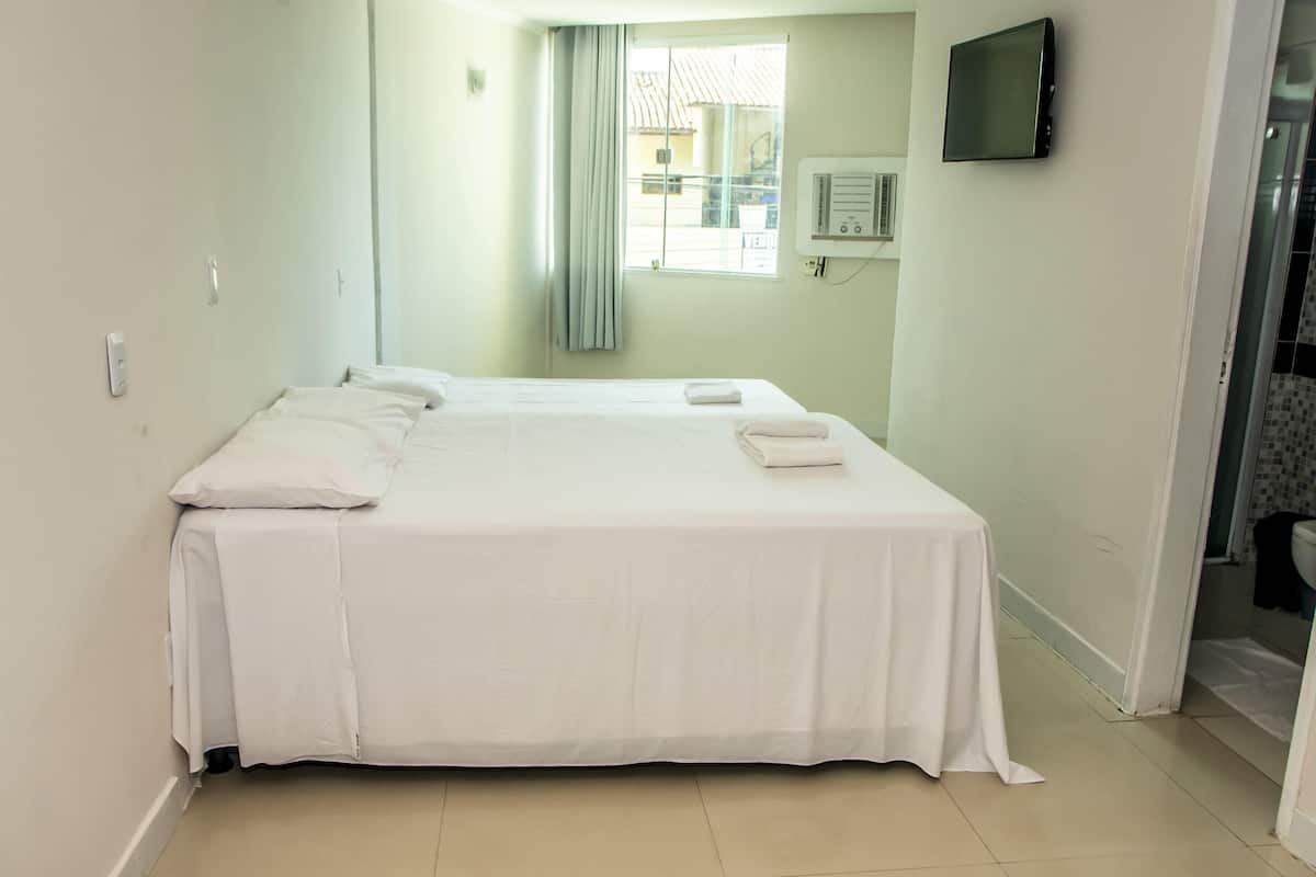 A clean, well-lit hotel room with a large bed, a flat-screen TV mounted on the wall, and a window with curtains.