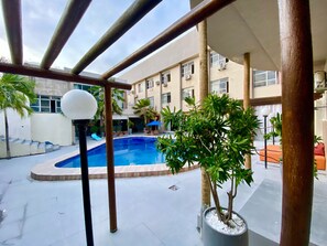 Un área de piscina con piscina azul cristalina, rodeada de plantas en macetas y mobiliario de exterior.