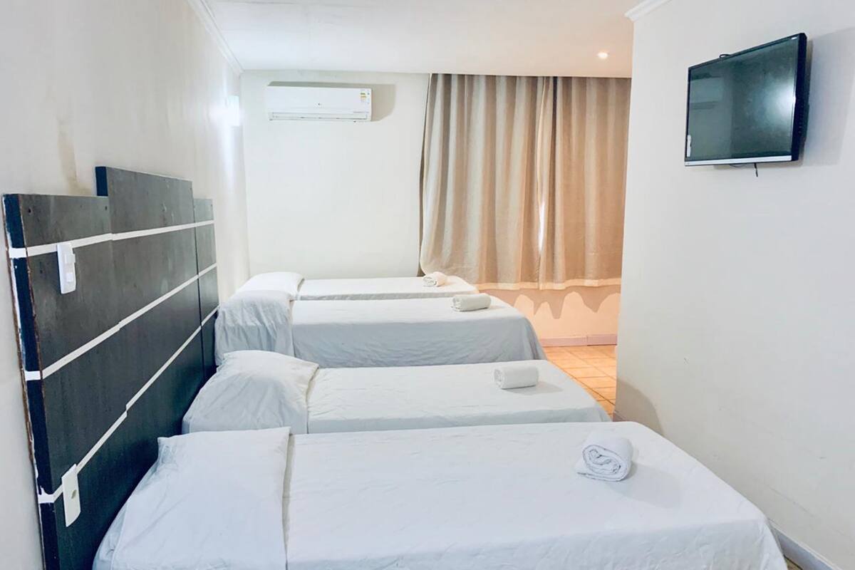A hotel room with three single beds, a flat-screen TV mounted on the wall, and an air conditioning unit on the wall.