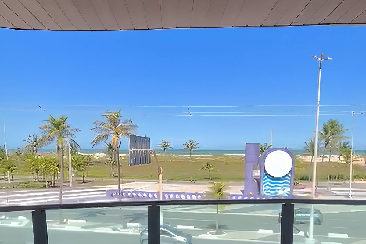 A view from a covered area with a clear sky, palm trees, and a road with vehicles.