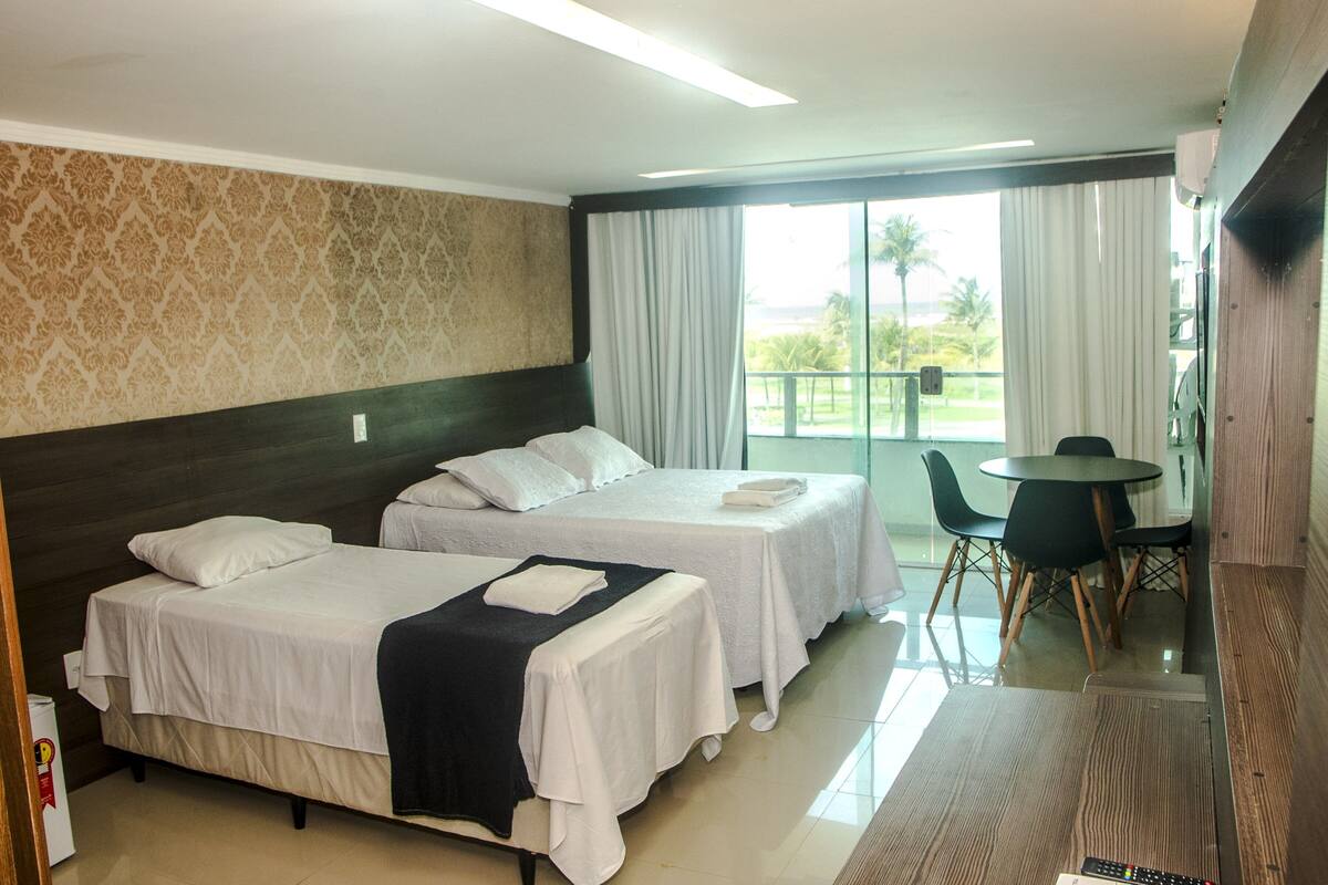 A hotel room with two beds, a dining area, and a view of the outdoors.
