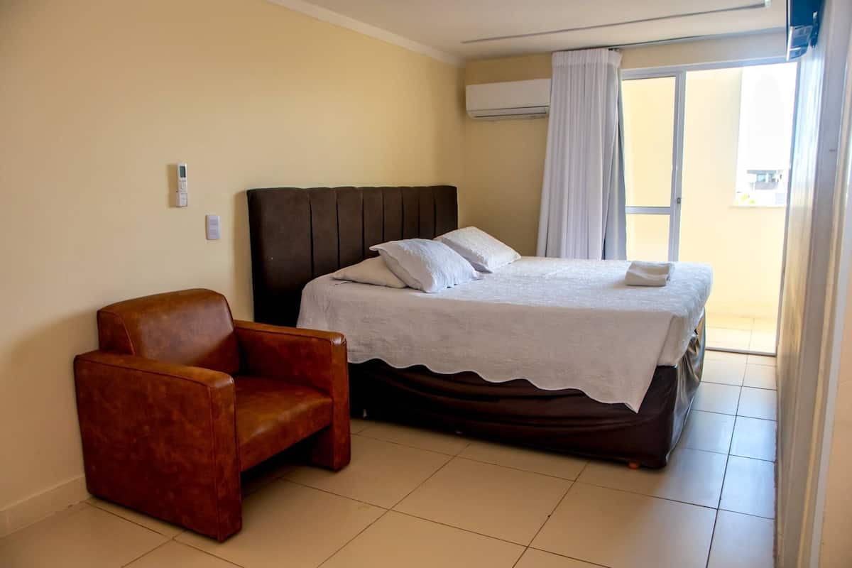 A hotel room with a bed, a chair, and a view of the outside.