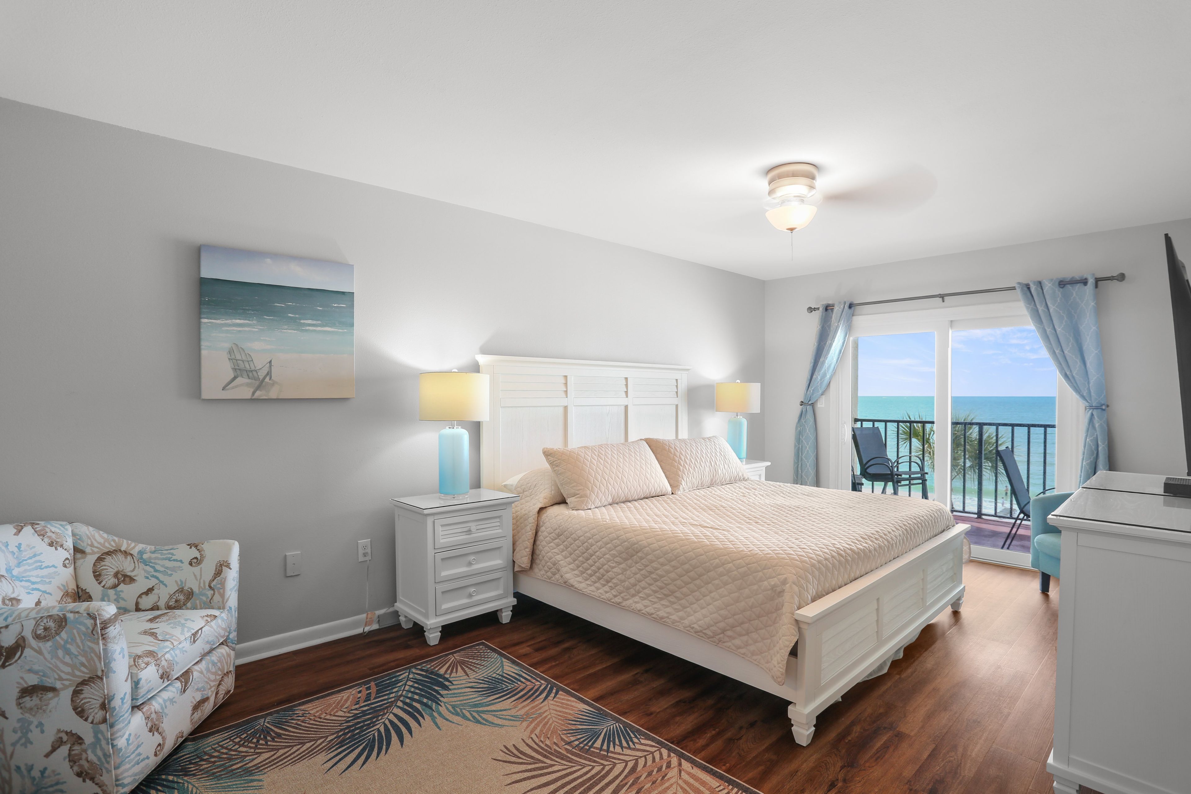 Quarto com cama, mesas de cabeceira, uma cadeira, um quadro e varanda com vista.