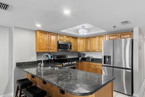 Uma cozinha moderna com bancadas de granito, eletrodomésticos de aço inoxidável, armários de madeira e uma ilha central com banquetas.