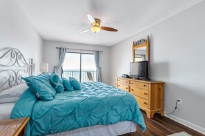 Quarto com cama, ventilador de teto, cômoda, televisão e janela com cortinas.