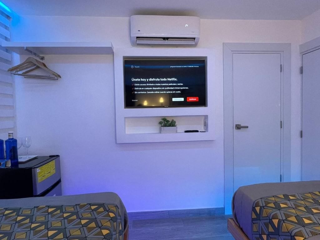 A hotel room with a mounted television displaying a Netflix interface, a door, and two beds with patterned bedding.