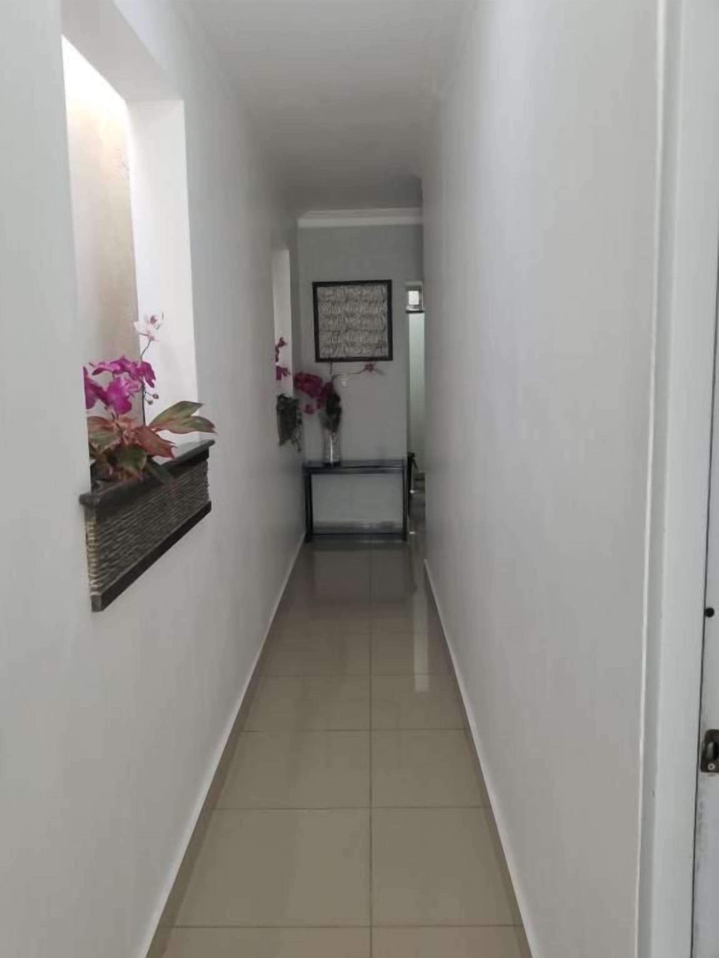 Un pasillo estrecho con suelo de baldosas, una puerta a la derecha y una pequeña mesa con un florero a la izquierda.