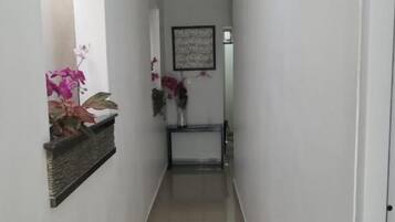 Un pasillo estrecho con suelo de baldosas, una puerta a la derecha y una pequeña mesa con un florero a la izquierda.