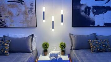 A modern hotel room with a bed, bedside tables, two potted plants, and artwork on the walls.