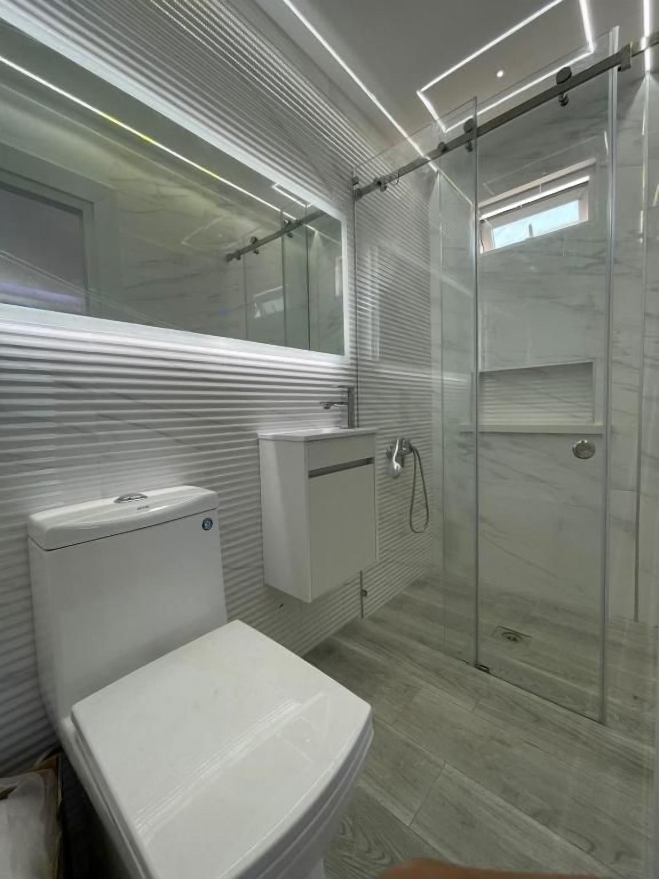 Un baño moderno con inodoro, lavamanos y cabina de ducha de vidrio.