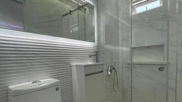 Un baño moderno con inodoro, lavamanos y cabina de ducha de vidrio.