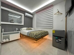 A modern bedroom with a built-in bed, a minibar, a wall-mounted TV, and a refrigerator.
