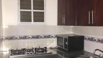 Cocina compacta con estufa a gas, microondas, fregadero y un refrigerador pequeño.