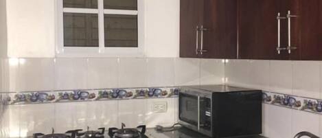 A compact kitchen with a gas stove, microwave, sink, and a small refrigerator.