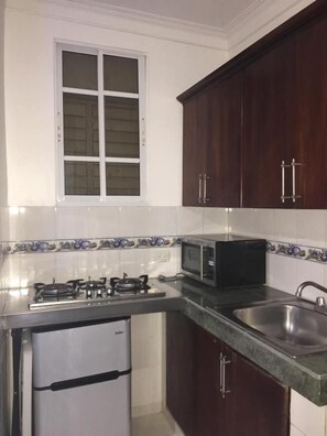 Cocina compacta con estufa a gas, microondas, fregadero y un refrigerador pequeño.