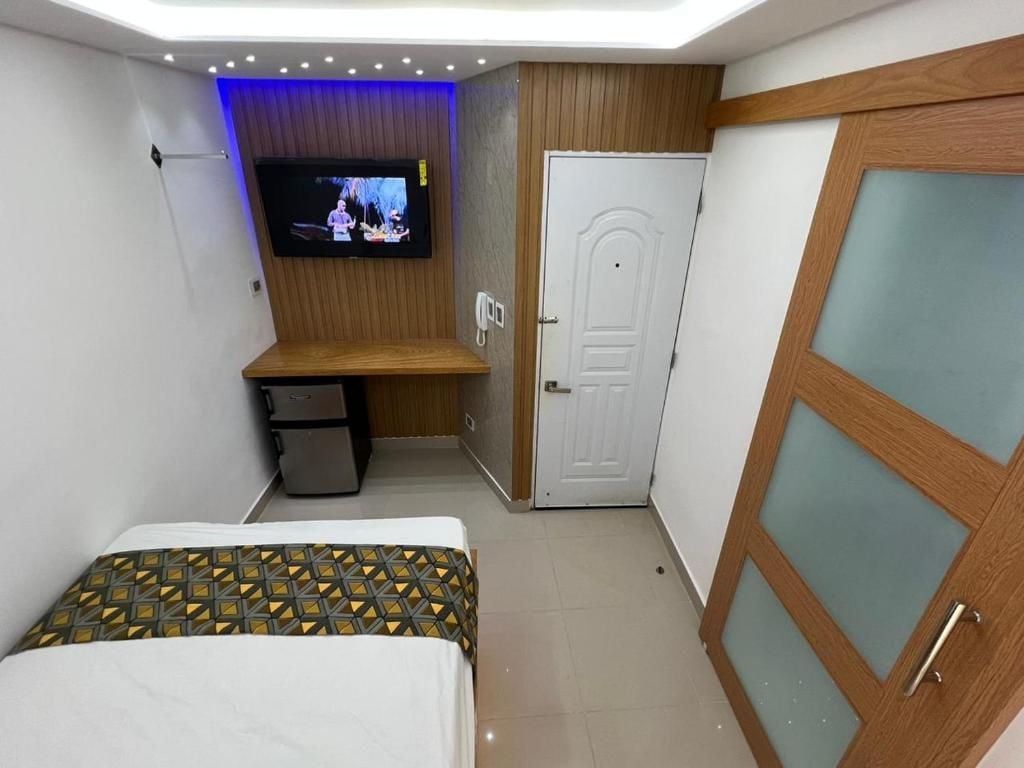 A hotel room with a bed, a TV mounted on the wall, a desk with a chair, and a wardrobe.