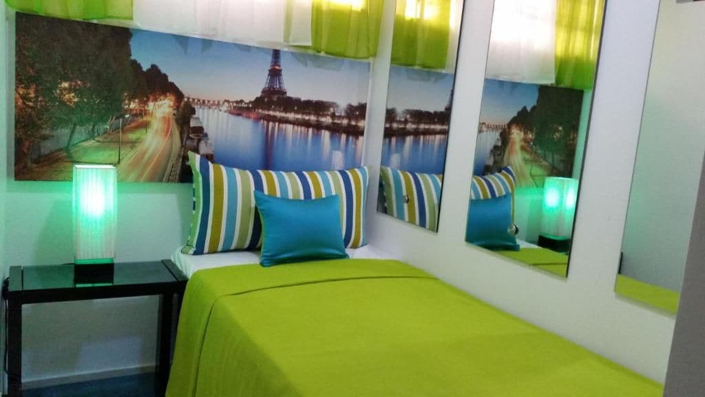 Ein Hotelzimmer mit Bett, Kissen, Nachttisch, Lampe und einer Wand mit Stadtbildgemälde und Spiegeln.