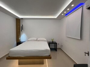 Un dormitorio moderno con cama suspendida, mesita de noche, televisor empotrado en la pared e iluminación de techo empotrada.