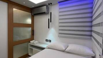 Moderni hotellihuone, jossa on sänky, yöpöytä ja sisäänrakennettu ilmastointilaite.