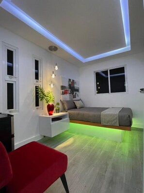 Un dormitorio moderno con una cama, una mesita de noche y una silla roja.