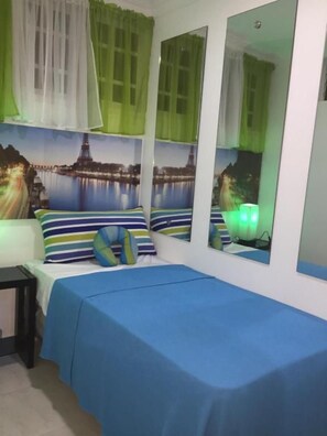 Un dormitorio con una cama, almohadas, una mesita de noche, un espejo y una lámpara de pared.