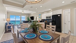 A spacious kitchen with white cabinets, a black refrigerator, and a dining area with a wooden table and blue placemats. - Treasure Island 0403 (Panama City Beach)