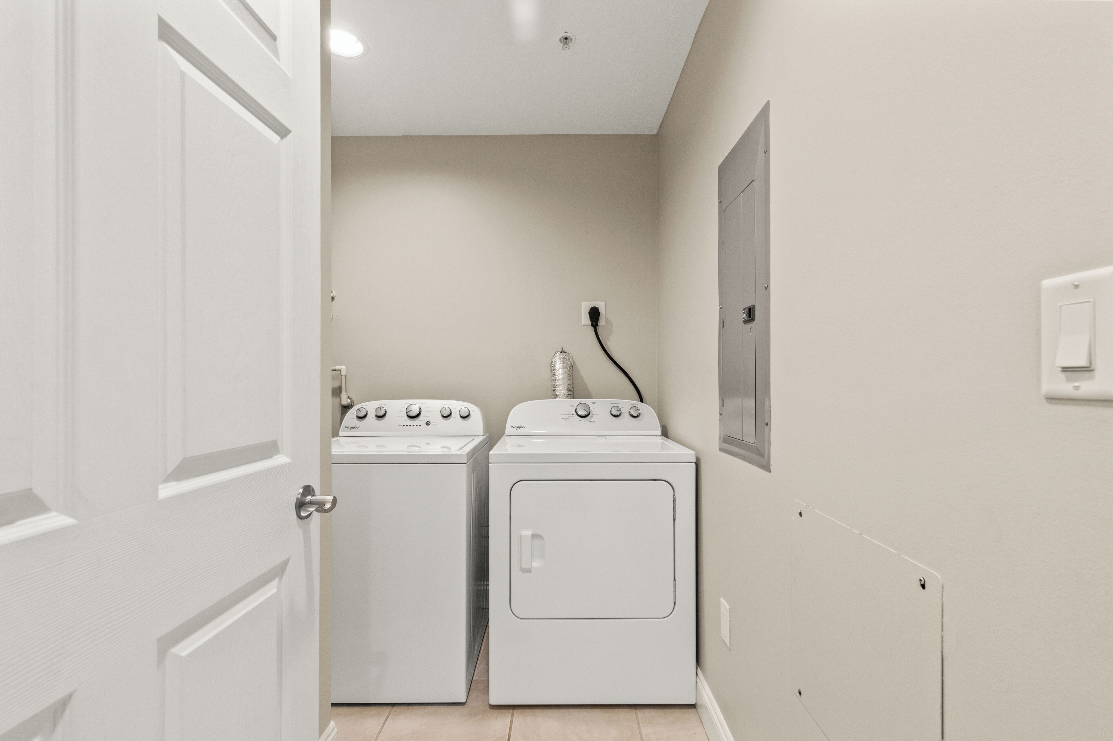 A laundry room with two white washing machines and a dryer, a white door, and a light switch on the wall.