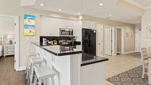 A modern kitchen with white cabinets, a central island with bar stools, stainless steel appliances, and recessed ceiling lighting. - Treasure Island 0403 (Panama City Beach)