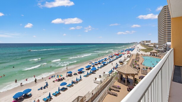 A beach resort with a long stretch of beach, a swimming pool, and a high-rise building in the background. - Treasure Island 0403 (Panama City Beach)