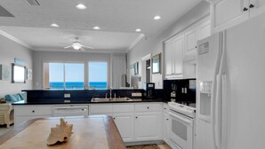 A modern kitchen with white cabinetry, a large island, and a view of the ocean through the windows. - Treasure Island 0305 (Panama City Beach)