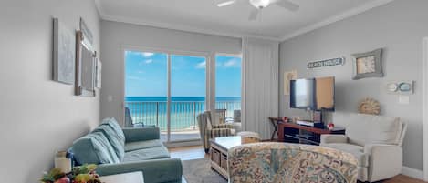 Ein Wohnzimmer mit Meerblick, einem Deckenventilator, einem Fernseher und einem Schild mit der Aufschrift 'BEACH HOUSE'.