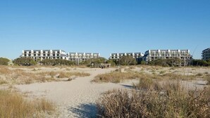 Een strandhotel met meerlaagsgebouwen, een zandpad dat naar de ingang leidt, en omliggende begroeiing langs het strand.
