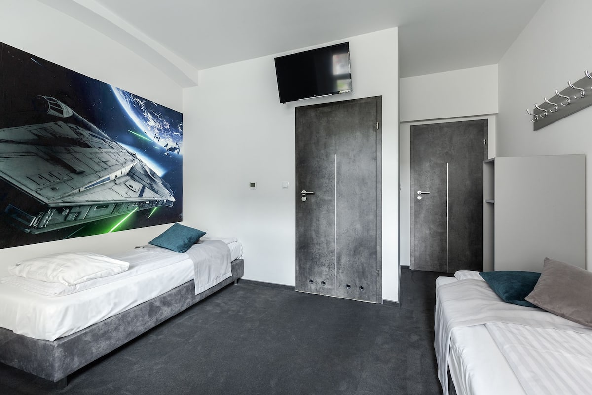 A modern bedroom with a large space-themed wall mural, a flat-screen TV, and a wardrobe.