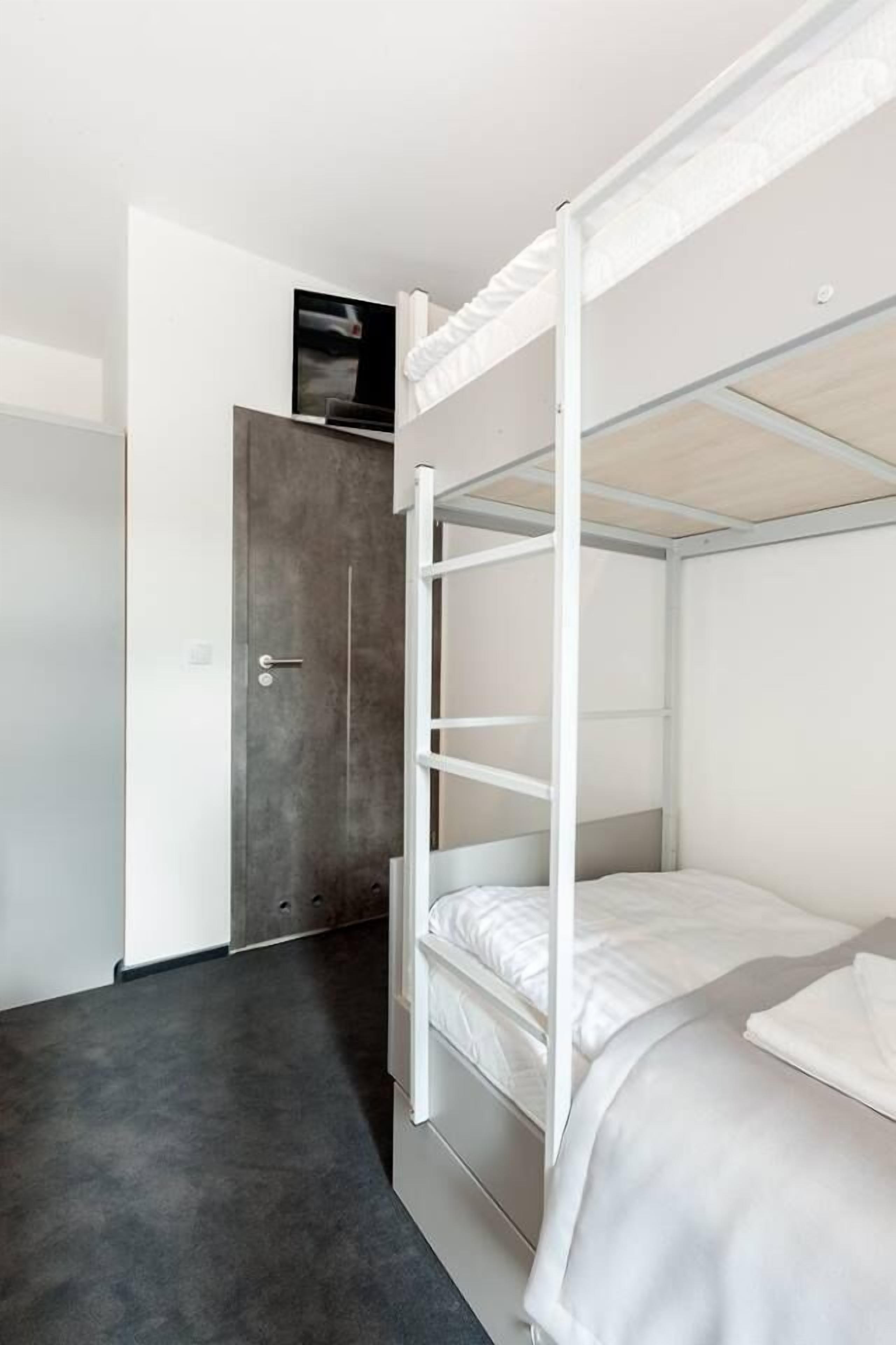 A bunk bed room with a door, a small TV on the wall, and a grey carpet.