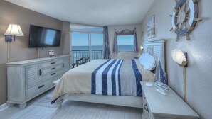 Une chambre à coucher comprenant un lit, une commode, un téléviseur, une fenêtre avec des rideaux et un élément de décoration représentant un gouvernail de bateau.