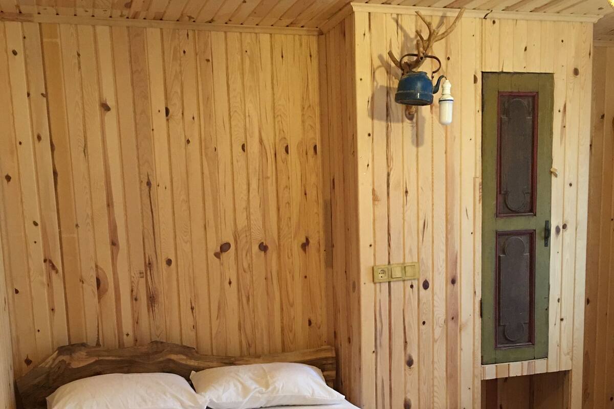 A wooden room with a bed, pillows, and a small table.