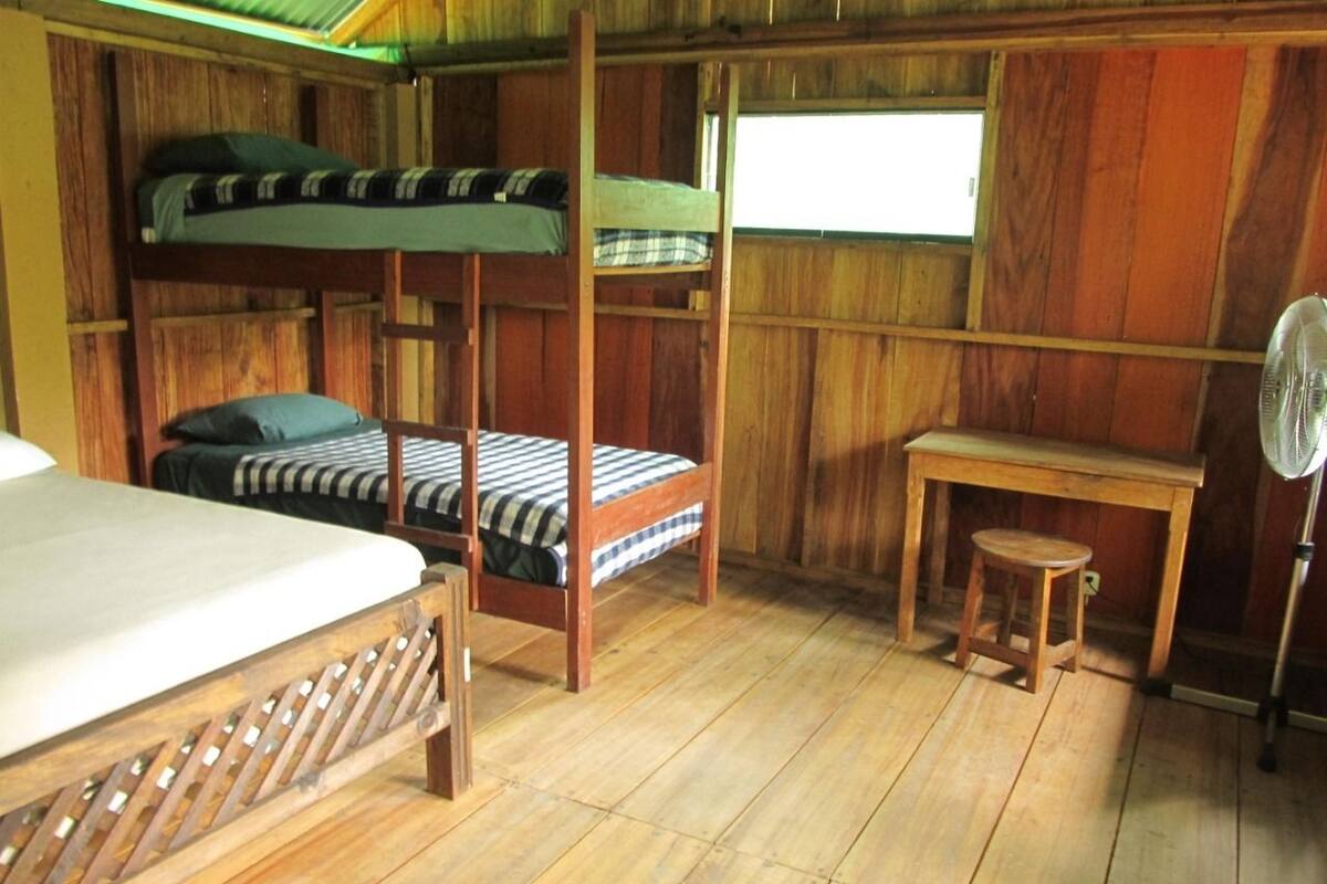 A wooden room with bunk beds, a small table, and a fan.
