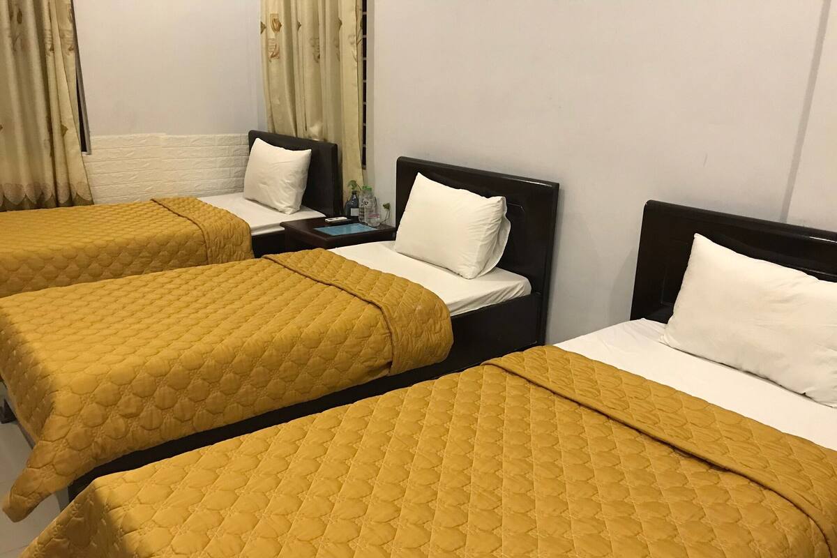 A hotel room with three single beds, each with a yellow quilted bedspread and white pillows.