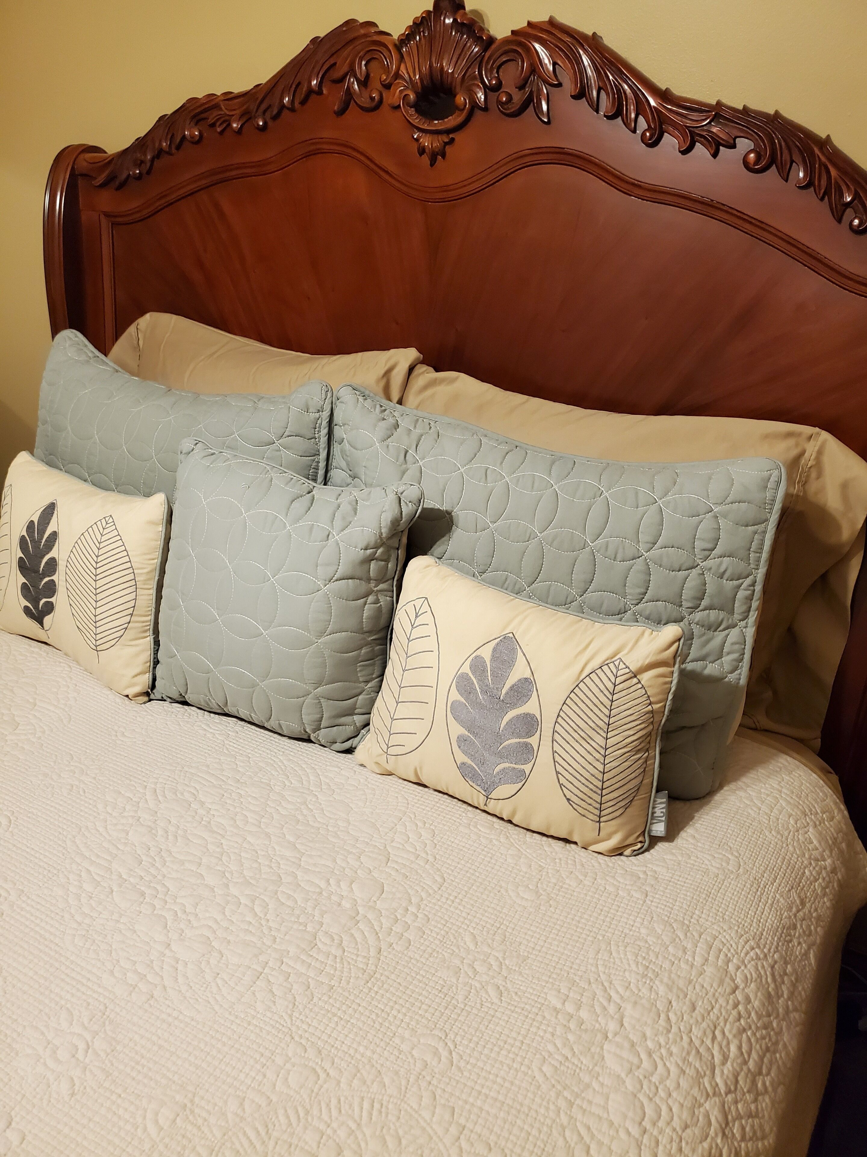 Una cama con cabecera de madera, varios cojines y una colcha blanca con textura.