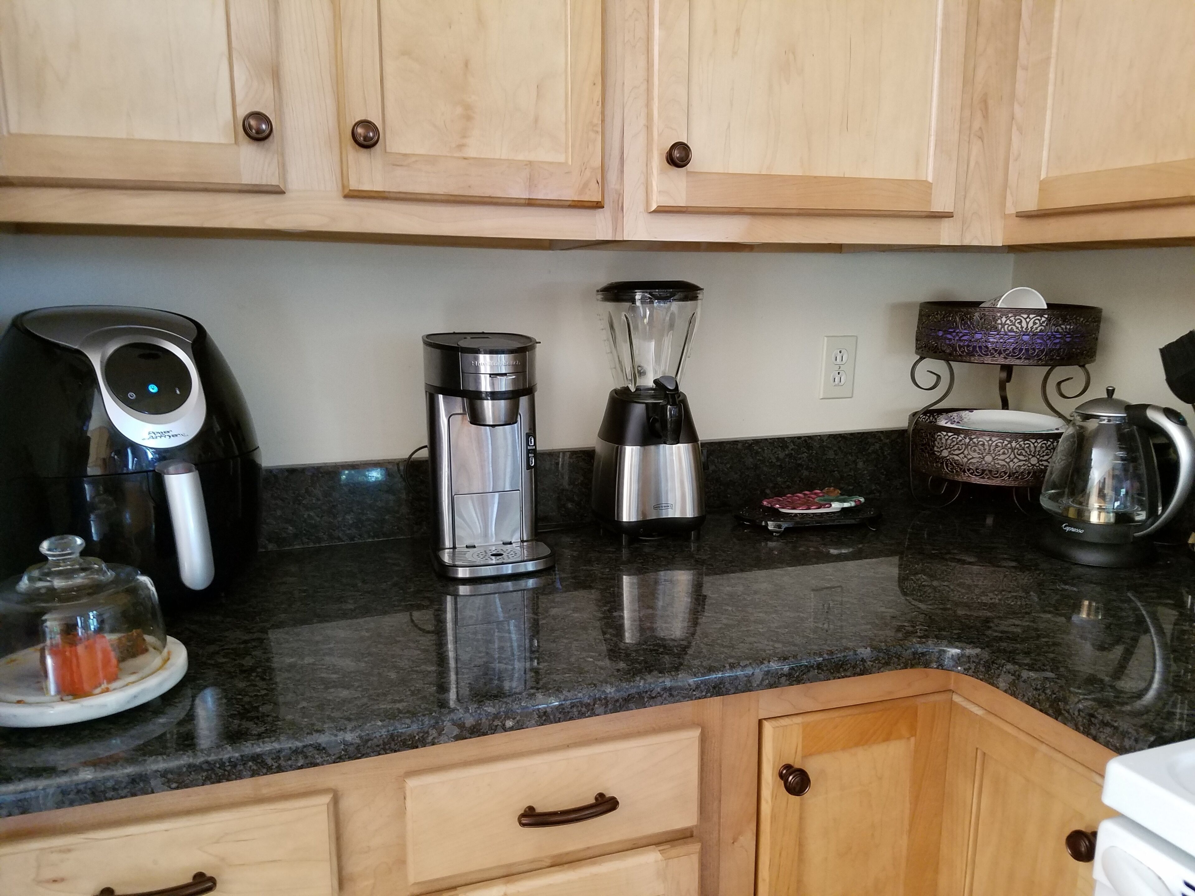 Een keuken met houten kastjes, een koffiezetapparaat, een blender, een waterkoker en een decoratief object op het aanrecht.