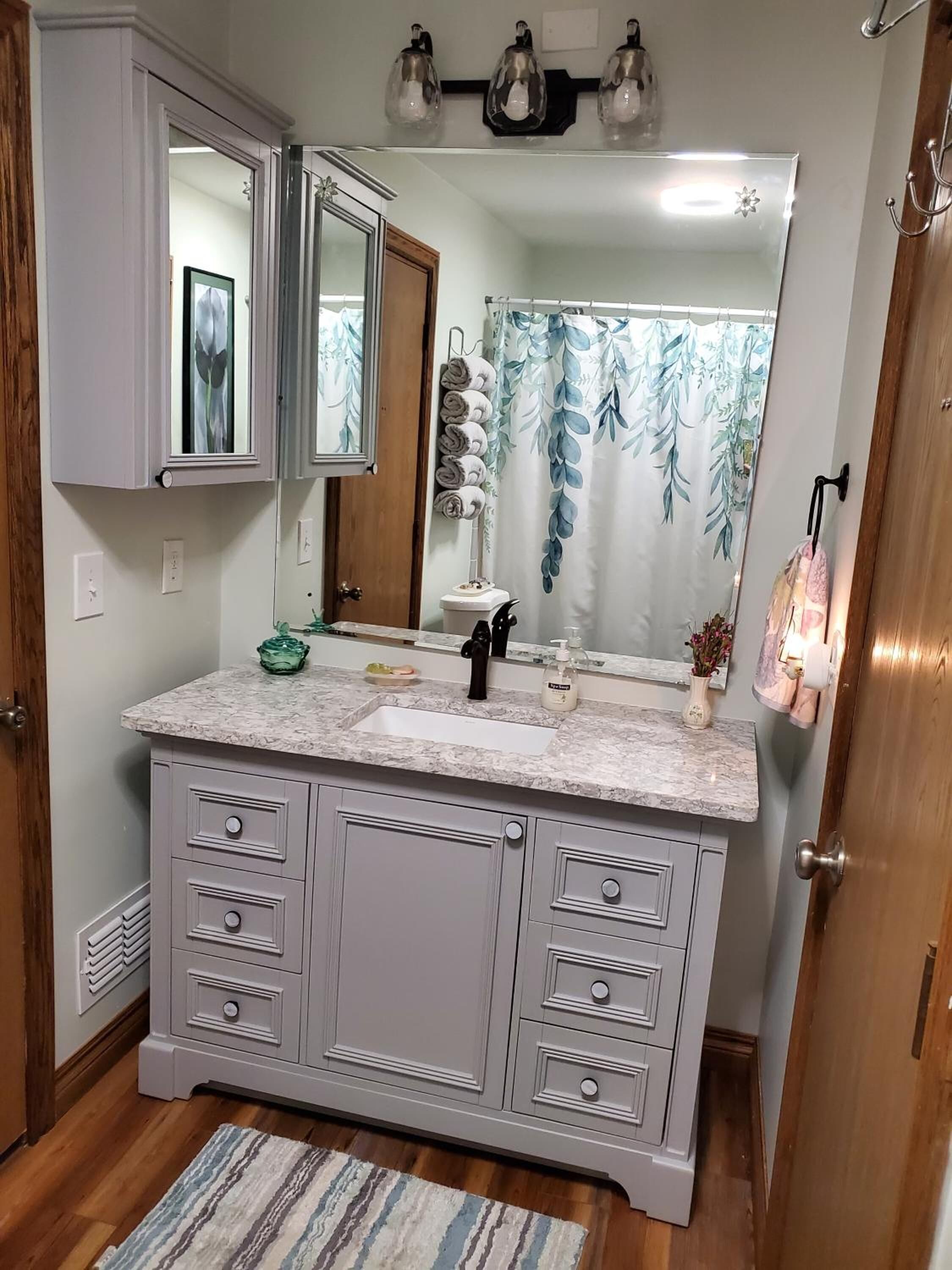 A bathroom with a marble sink, a large mirror, and a shower curtain with a leaf pattern.