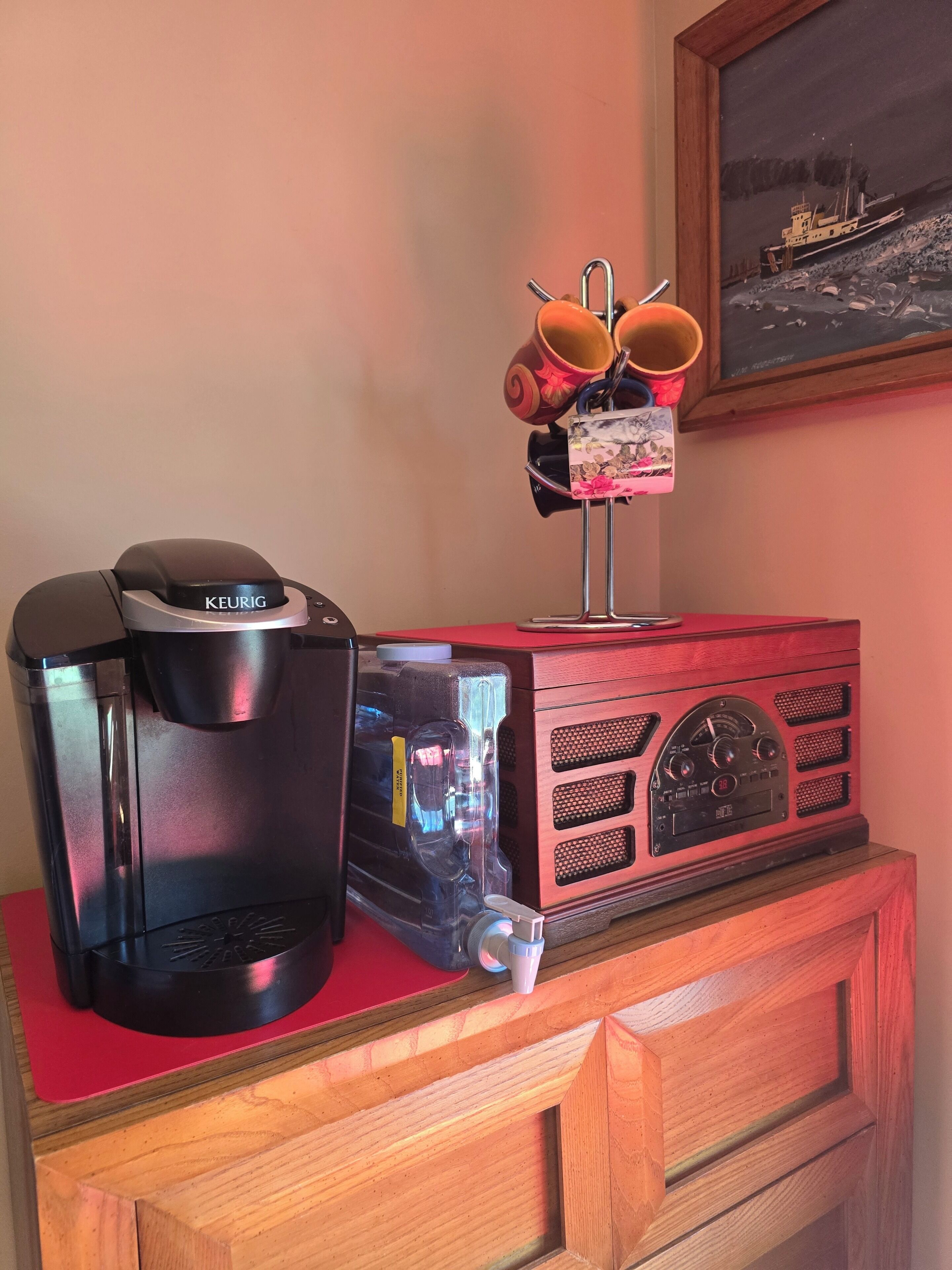 A coffee maker, a water dispenser, and a radio on a wooden cabinet.