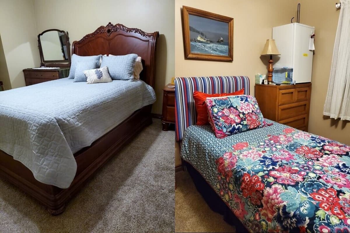 A bedroom with a wooden bed, a nightstand, a dresser, a mirror, a framed picture on the wall, and a refrigerator.