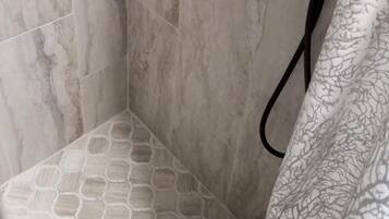 A shower area with a tiled floor, a showerhead, and a wall-mounted control panel.
